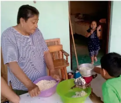 Persona adulta preparando alimentos en una mesa con niños presentes; foto de Jesús Eduardo Arteaga Flores, Tamaulipas.