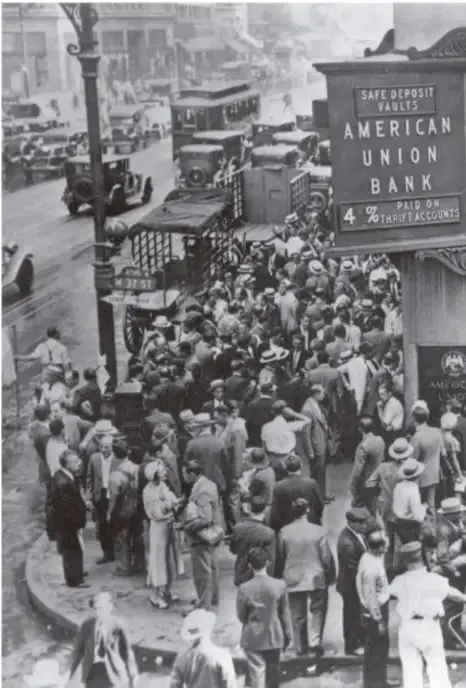 Fotografía en blanco y negro de una multitud frente al American Union Bank en Nueva York, con un letrero que dice 'SAFE DEPOSIT VAULTS' y '4% PAID ON THRIFT ACCOUNTS', durante la crisis bancaria de 1929.