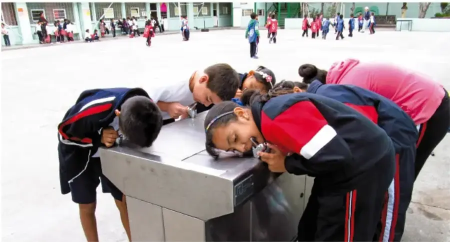 Estudiantes de primaria observando y manipulando objetos sobre una superficie metálica en el patio escolar.