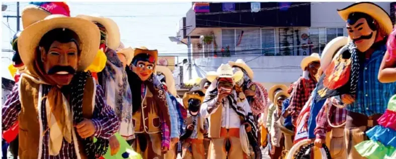 Fotografía de un desfile o carnaval con personas disfrazadas con sombreros de paja, máscaras y trajes coloridos, representando una expresión cultural tradicional.