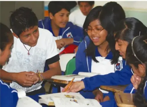 Fotografía de estudiantes de secundaria trabajando en equipo alrededor de un pupitre con materiales del experimento.
