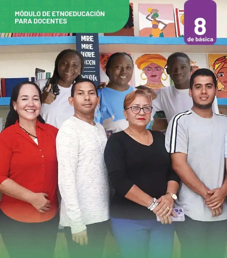 Fotografía grupal de siete personas (docentes y estudiantes afroecuatorianos) sonrientes en un espacio educativo con estanterías de libros y retratos artísticos de mujeres afrodescendientes al fondo.