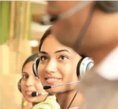 Fotografía de mujeres jóvenes con micrófonos y auriculares atendiendo llamadas en un centro de atención telefónica, ilustrando el empleo bilingüe mencionado en el texto.