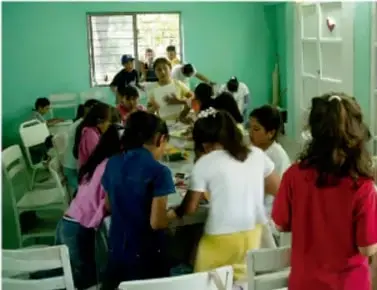 Estudiantes en un aula trabajando en equipo alrededor de mesas, dialogando sobre el proyecto.
