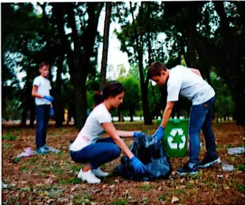 Niños voluntarios recogen basura en un parque y la colocan en un recipiente de reciclaje.