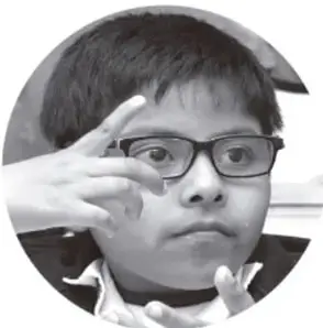 Fotografía de un niño con lentes haciendo una seña con la mano.