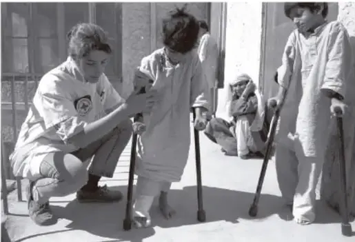 Fotografía en blanco y negro que muestra a un enfermero atendiendo a un niño con muletas, y otro niño de pie con muletas. Parecen estar en un entorno de atención médica o rehabilitación.