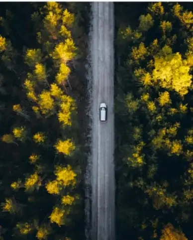 Vista aérea de un camino en un bosque con un vehículo blanco.