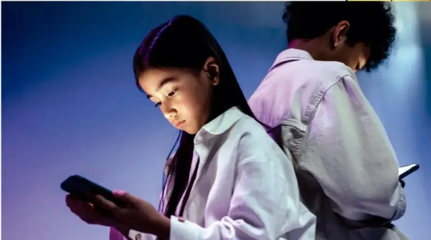 Fotografía de dos niñas usando teléfonos celulares en un ambiente con luz azulada.