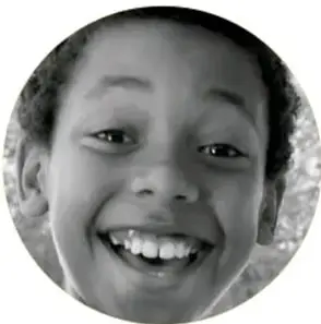 Fotografía circular en blanco y negro de un niño de rostro sonriente, con dientes visibles, que mira hacia arriba con alegría.