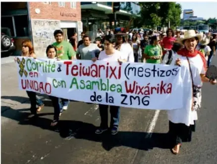 Marcha con una manta que dice "Comité Teiwaríxi (mestizos) en UNIDAD con Asamblea Wixárika de la ZMG".