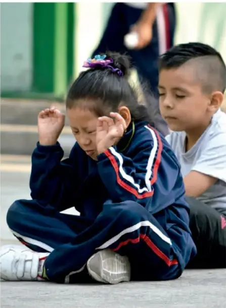 Fotografía de una niña y un niño sentados en el suelo con los ojos cerrados, en actitud de relajación o meditación.