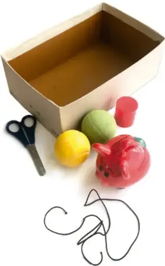 Caja de zapatos abierta con tijeras, pelotas de colores, un juguete y un cordón enredado alrededor.