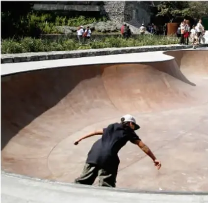 Persona haciendo skateboard en una pista de concreto con espectadores alrededor.