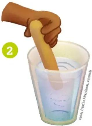 Mano sosteniendo un abatelenguas dentro de un vaso con agua y sal.