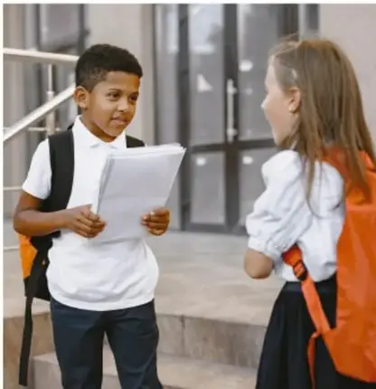 Fotografía de dos niños escolares conversando, uno con uniforme y otro con mochila, representando a Martha y Rodrigo.