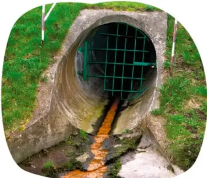 Tubería de drenaje vertiendo agua residuales de color oscuro hacia el exterior.