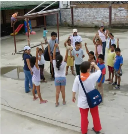 Grupo de niños y niñas en el patio de la escuela, algunos con los brazos en alto, participando en una actividad grupal.