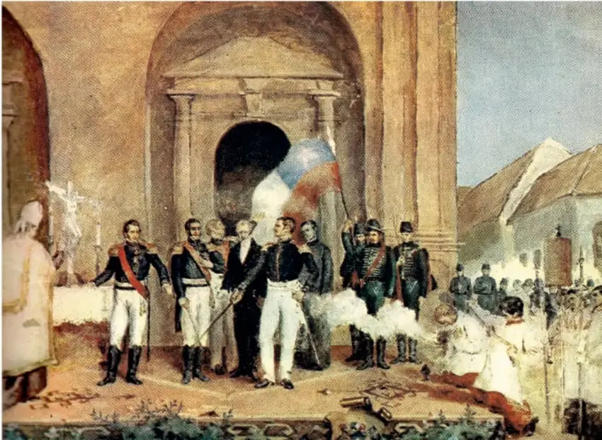 Pintura histórica de la ceremonia de la Independencia de México: figuras militares con uniformes y bandera tricolor, clérigos, pueblo presente y arquitectura colonial al fondo; al pie, restos o instrumentos en el suelo que sugieren el episodio de los llamados «dormidos de Dolores».