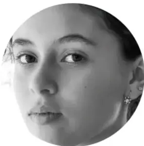 Fotografía en blanco y negro del rostro de una estudiante que observa de frente, con aretes pequeños.