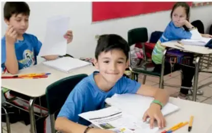 Manos de estudiantes manipulando frascos de vidrio con líquidos de colores y palitos, en una actividad práctica.