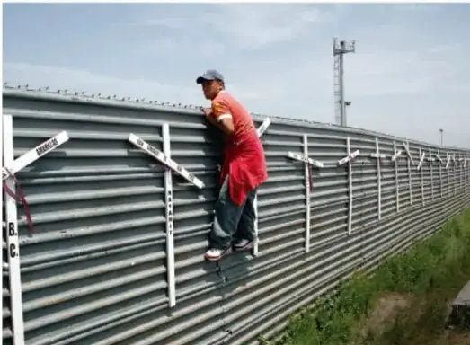 Fotografía de un trabajador con camisa roja y gorra subiendo una estructura metálica de una vivienda en construcción, con cielo nublado de fondo.