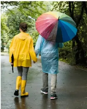 Fotografía de dos personas caminando bajo la lluvia con impermeables amarillo y azul y una sombrilla multicolor.