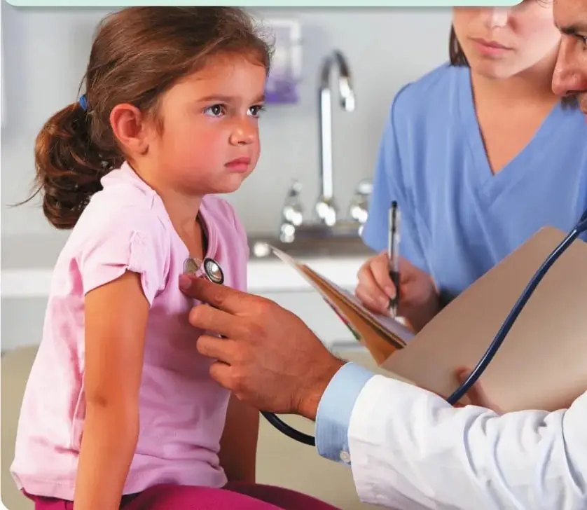 Una niña visita a un pediatra en un consultorio médico. Una profesional de la salud registra información mientras un médico examina a la niña.