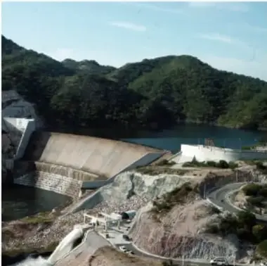 Foto aérea de una presa de arco con vertederos en un embalse rodeado de vegetación.