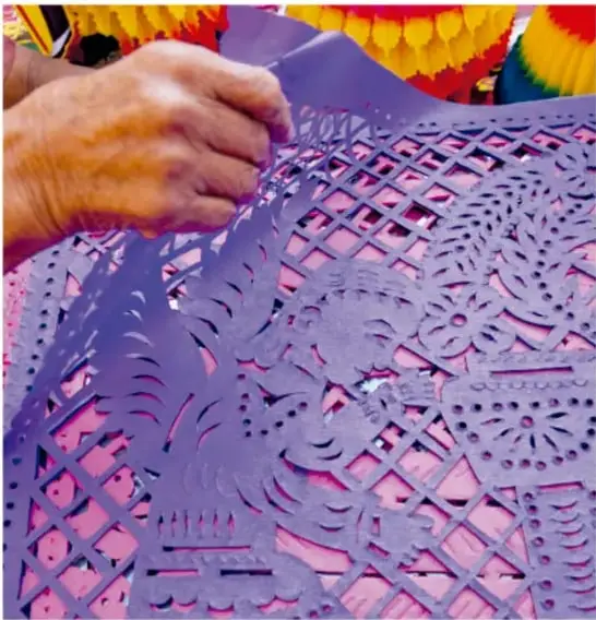 Fotografía de una calaverita de azúcar decorada de colores sobre papel picado rosa y amarillo.