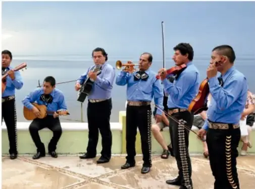 Grupo de mariachis tocando instrumentos junto al mar.