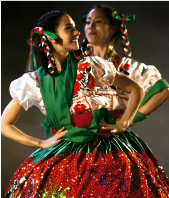 Fotografía de dos bailarinas con vestidos tradicionales de colores vivos (rojo, verde y blanco) con moños en el cabello, representando la danza folclórica o regional.