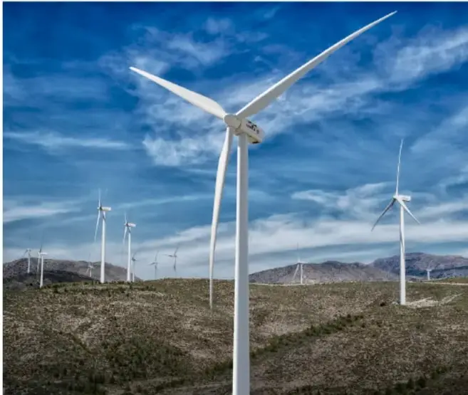 Fotografía de un parque eólico con varios aerogeneradores blancos sobre un paisaje árido y cielo azul con nubes, como ejemplo de energía renovable.
