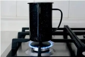 Pocillo oscuro sobre una estufa de gas con llama, calentando la mezcla para evaporar el agua.
