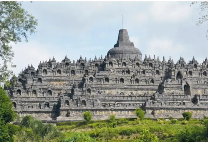 Fotografía del templo de Borobudur con sus terrazas escalonadas, estupas con forma de campana y el gran estupa central, rodeado de árboles.