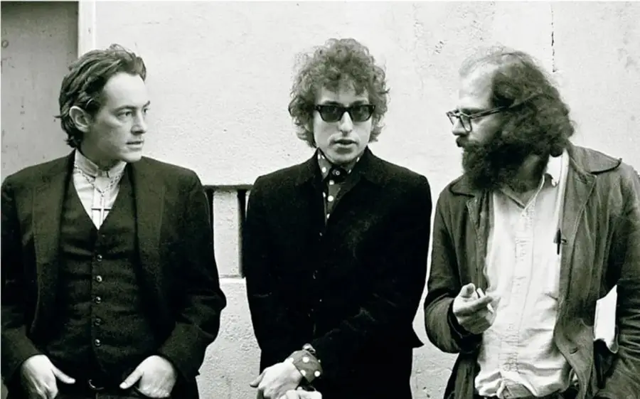 Fotografía en blanco y negro de tres hombres jóvenes con vestimenta de los años sesenta; el del centro usa lentes oscuros y cabello rizado, el de la derecha tiene barba y sostiene un cigarrillo.
