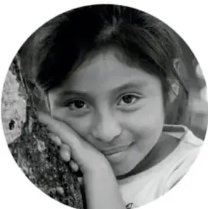 Fotografía en blanco y negro de una niña sonriente apoyada sobre una superficie, con una mano en el rostro.