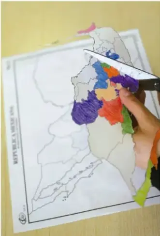 Mano de un estudiante coloreando un mapa de las regiones de México con distintos colores.