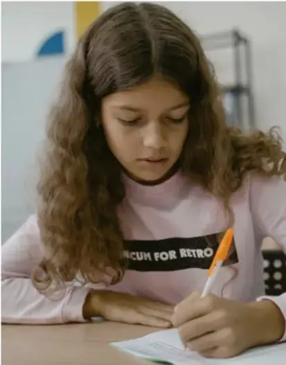 Fotografía de una estudiante escribiendo en una libreta con un lápiz, concentrada en su trabajo de planificación.