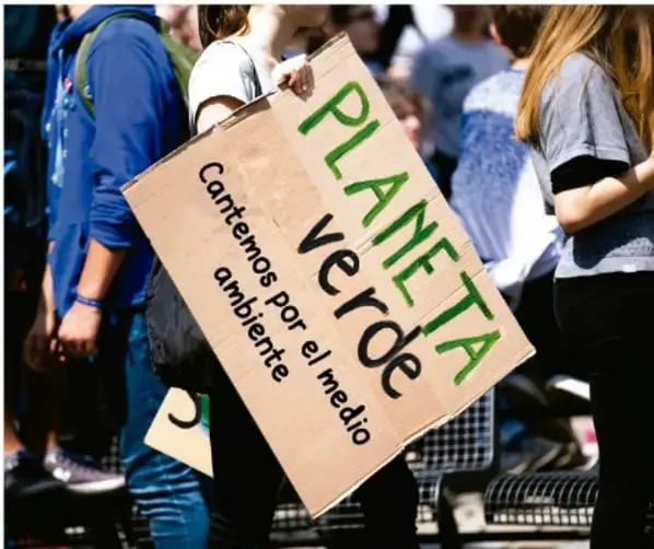 Manifestantes sostienen una pancarta de cartón que dice “PLANETA VERDE — Cantemos por el medio ambiente” en una movilización juvenil.