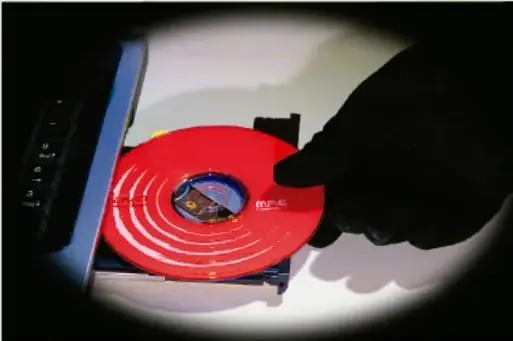 Mano enguantada insertando un disco compacto rojo en una unidad, representando la suplantación de identidad o acceso ilícito a datos.