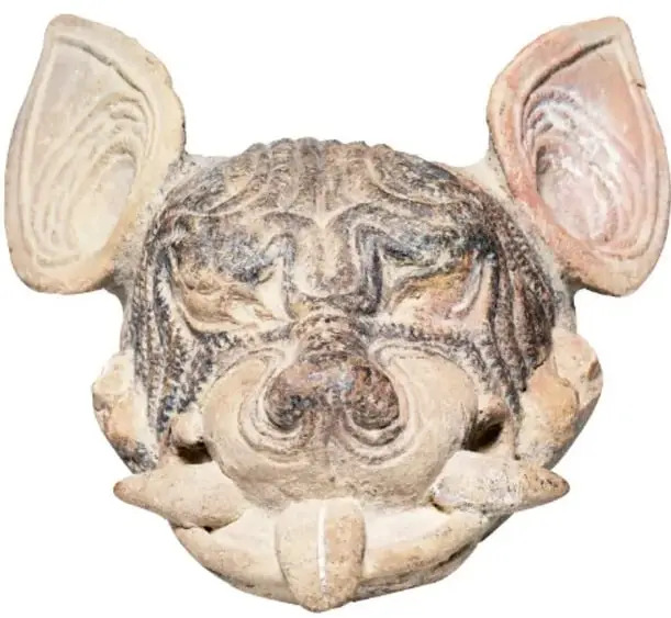 Escultura o figurilla prehispánica de barro que representa la cabeza de un perro, con orejas grandes y dientes salientes, probablemente un xoloitzcuintle.