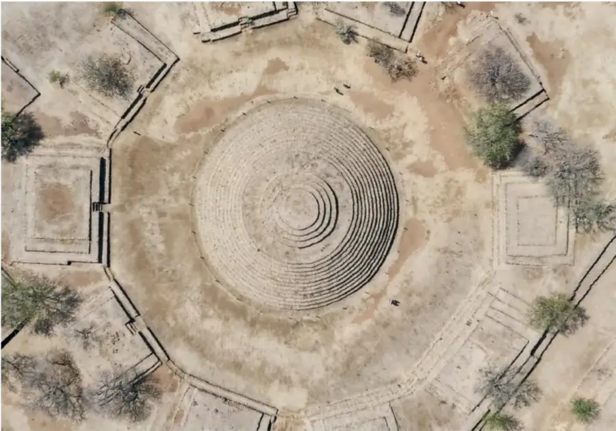 Vista aérea del sitio arqueológico de Guachimontones: una gran pirámide circular concéntrica (huachimontón) en el centro, rodeada de plataformas cuadrangulares y vegetación seca.