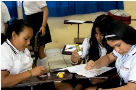 Fotografía de estudiantes de telesecundaria trabajando en equipo en el aula, elaborando materiales del proyecto con papel y colores.