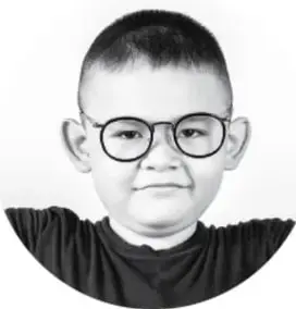 Fotografía en blanco y negro de un niño con lentes que sonríe, apoyando las manos sobre una superficie.