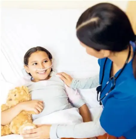 Fotografía de una médica atendiendo a una niña sonriente que sostiene un peluche, en un entorno hospitalario.
