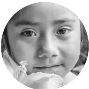 Fotografía en blanco y negro de una niña de primaria apoyando el rostro con la mano, de tamaño circular.