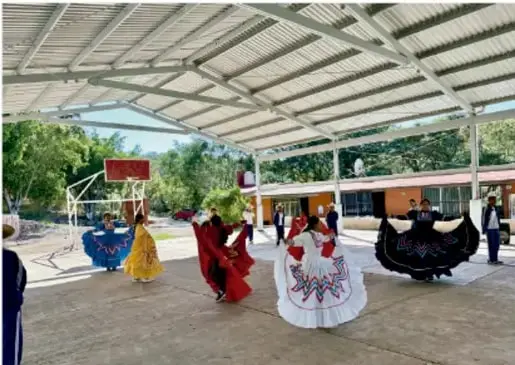 Fotografía de estudiantes con vestidos tradicionales coloridos realizando una presentación de danza en un patio techado de la escuela, probablemente durante la exhibición de arte del proyecto.