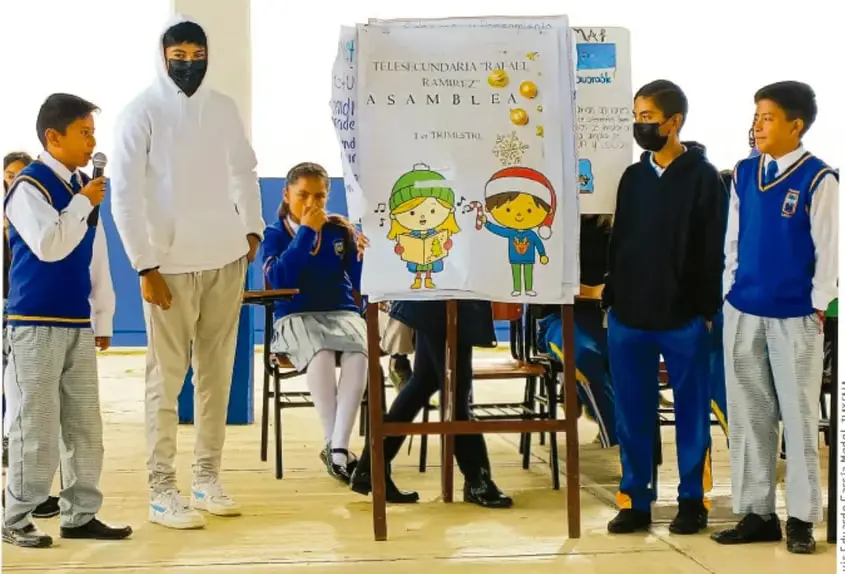 Fotografía de estudiantes de Telesecundaria junto con su maestro presentando un rotafolio sobre la asamblea de 1er trimestre, con recortes y dibujos.