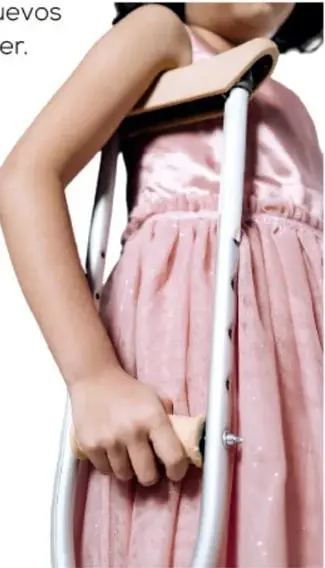Fotografía de una niña con vestido rosa usando muletas, sosteniendo una de ellas con la mano derecha.